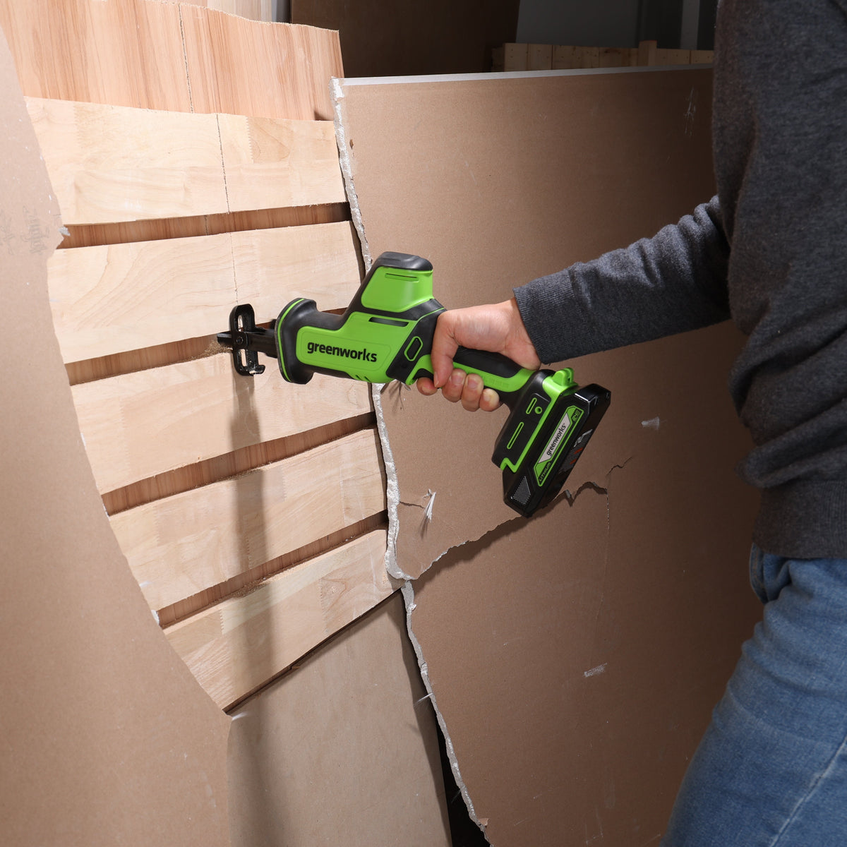 Person using a green and black power tool on wooden panels.